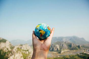 Man holding globe facing mountain. 