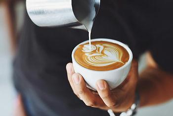 Man pouring steamed milk and foam into a cappuccino.